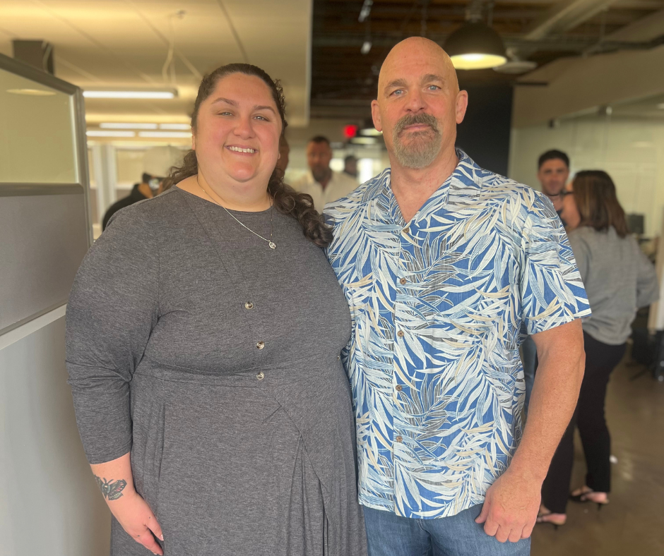 Hailey Cook and Tim Lawless smile side by side after learning about their recent promotions at VetComm, celebrating their career growth together.
