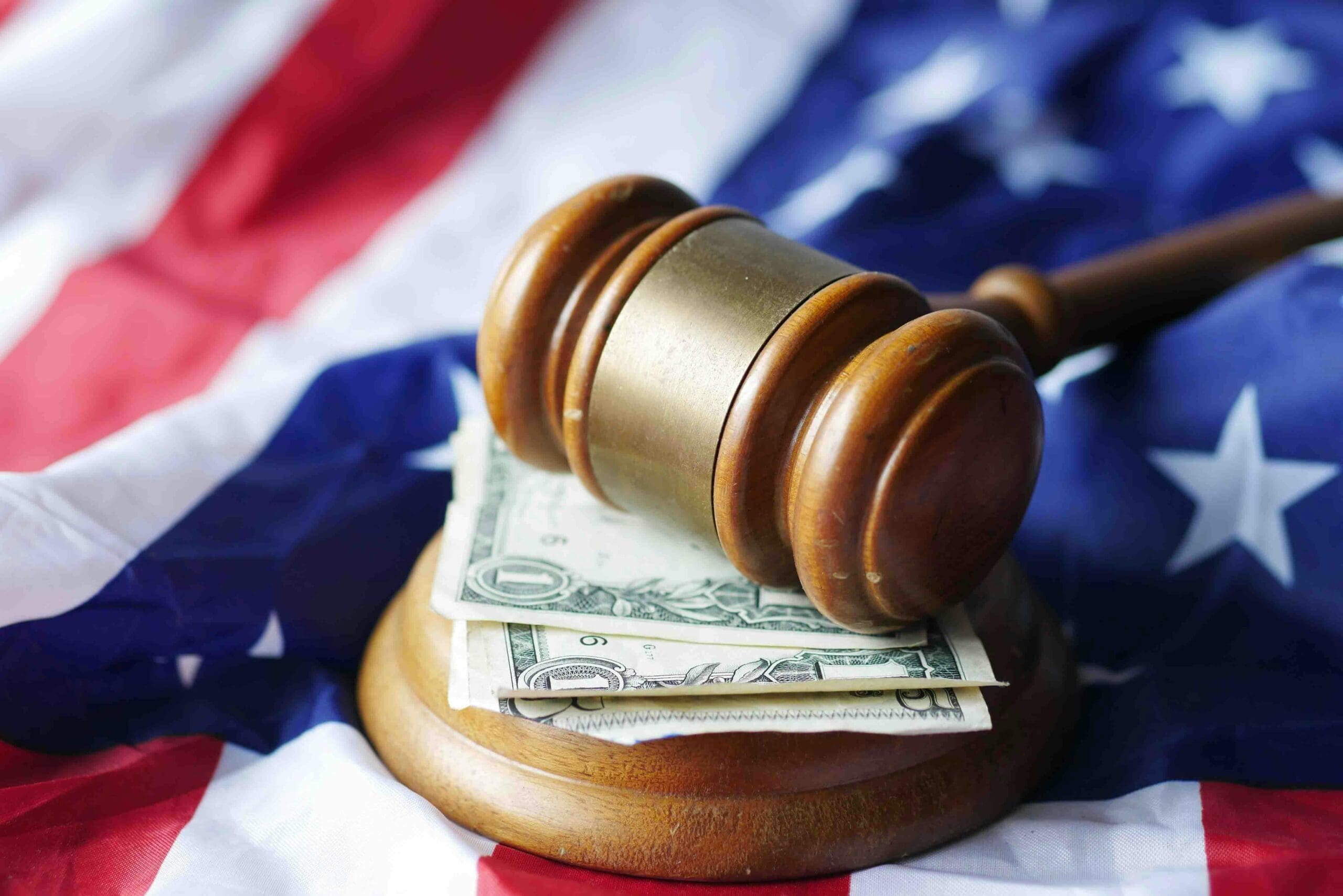 A judge’s gavel resting on dollar bills with an American flag in the background.